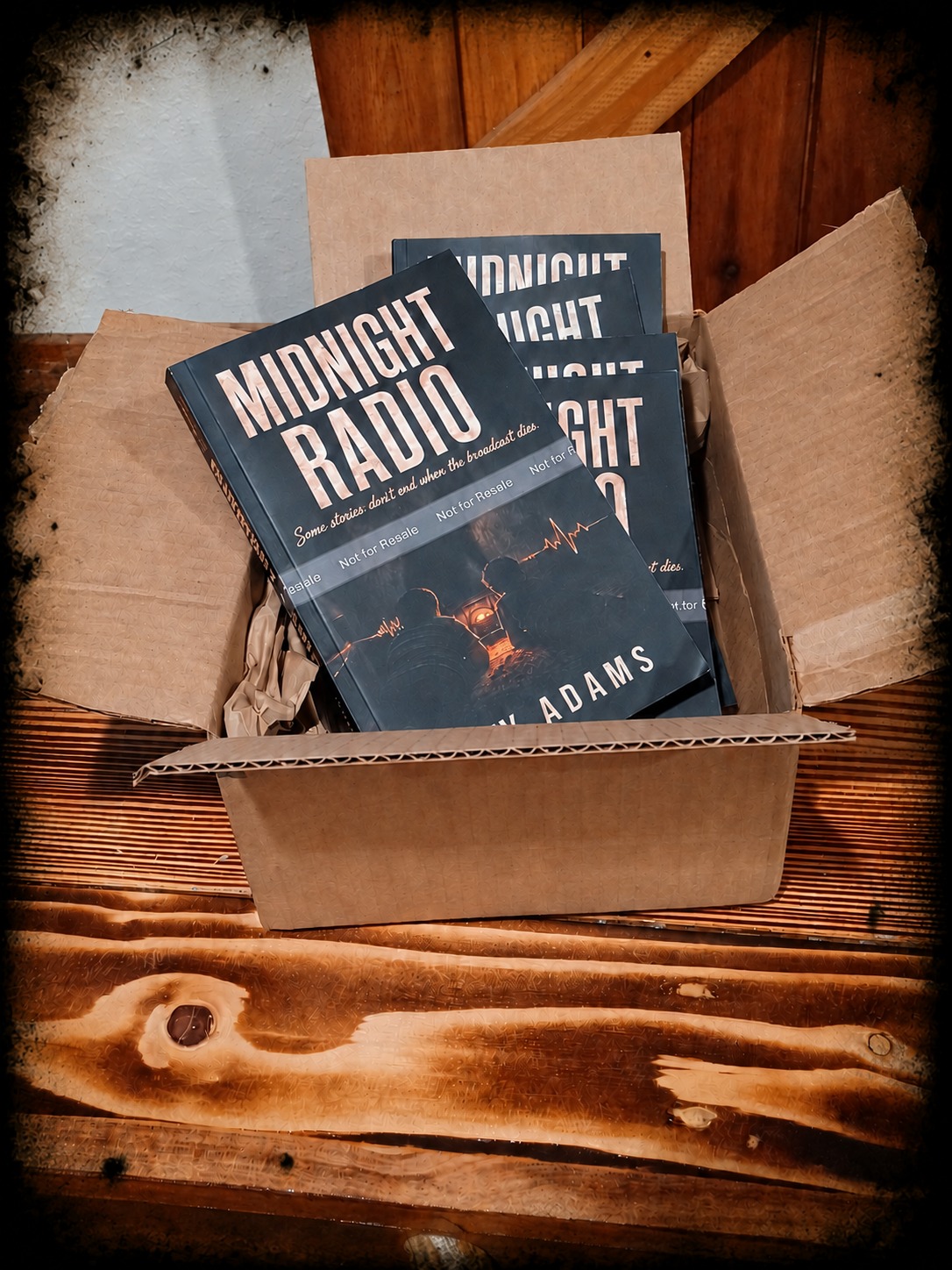 An open plain brown box holding Midnight Radio proof copies on a wooden table.