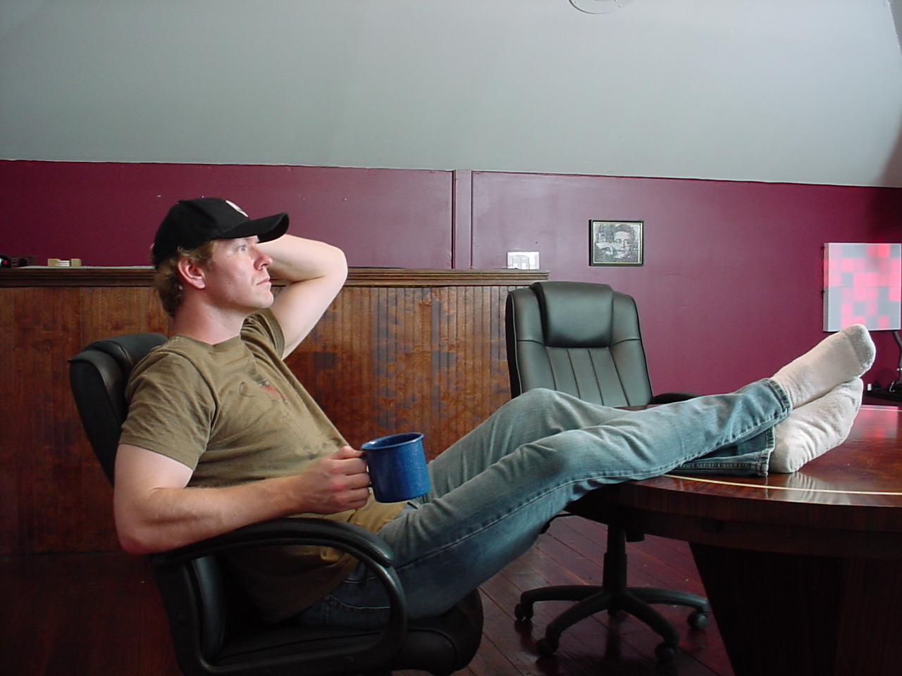 Jerry Adams in a black hat, holding a coffee mug with his feet on a table, when he first started Midnight Radio.
