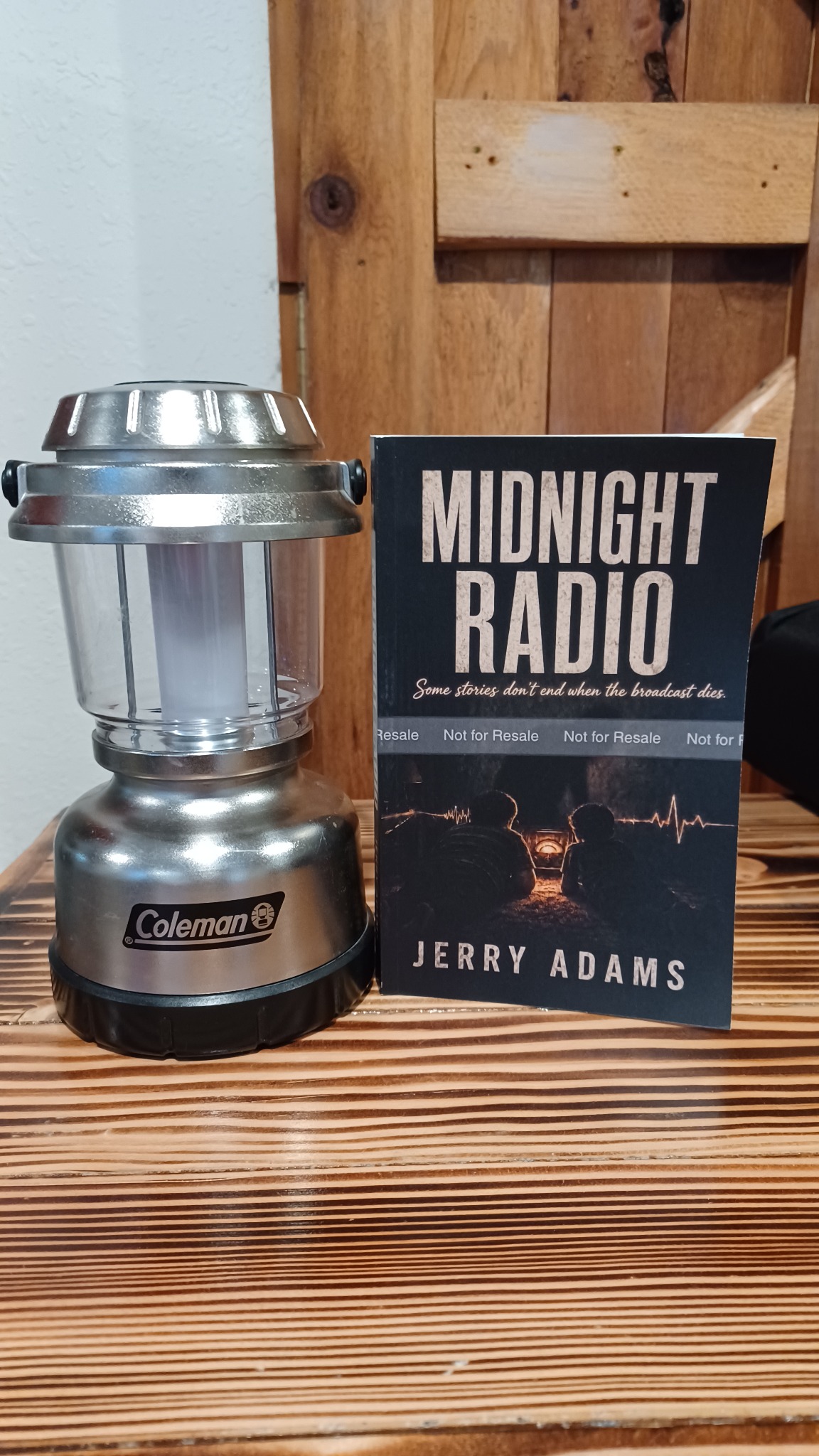 A silver Coleman lantern beside a Midnight Radio proof copy, both against a wooden backdrop.